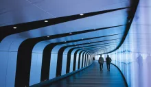Two men walking down a long, curved hallway lit in blueish purple.
